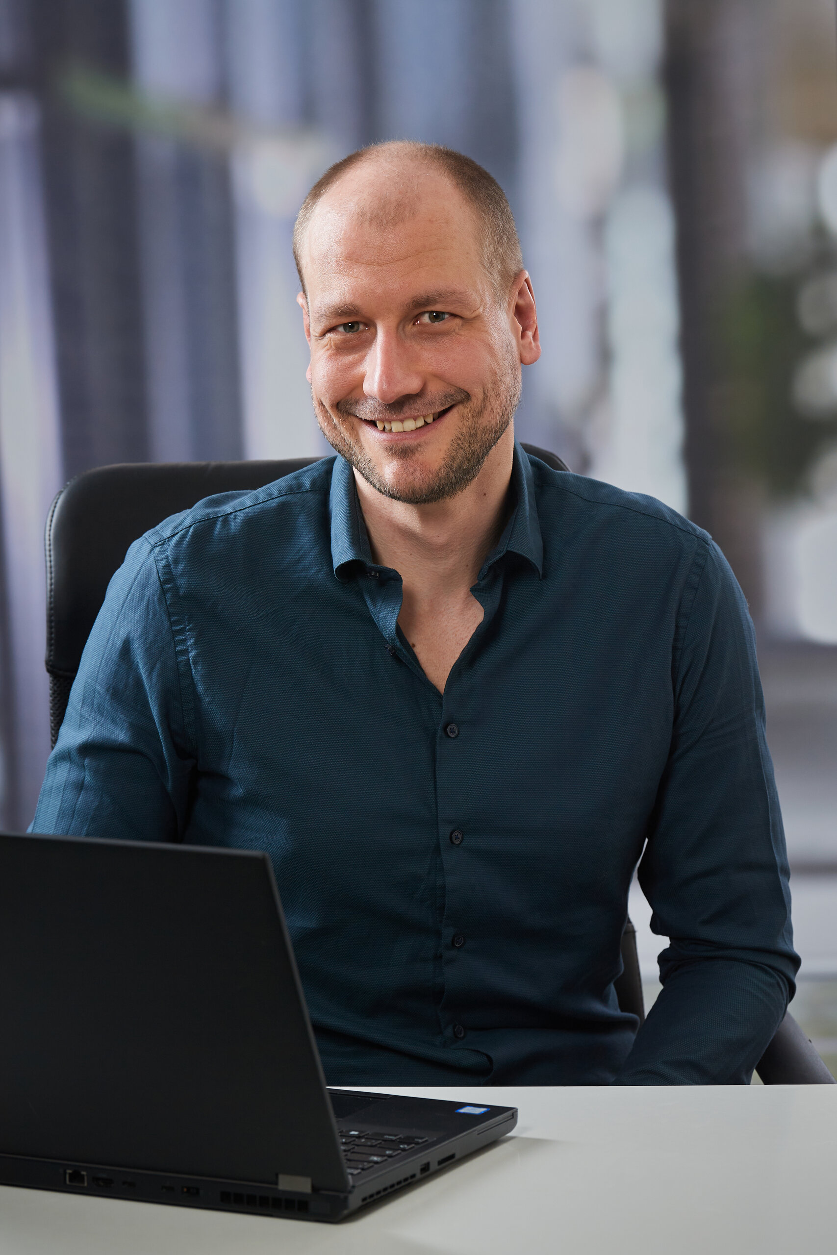 Ein Portrait sitzend am Laptop mit hellem Hintergrund von Christopher Schulz
